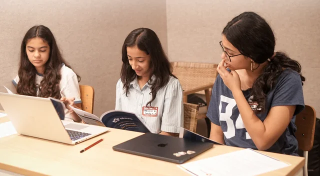 Students collaborating with workshop packets and laptops
